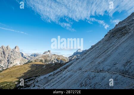 Dramatic footpath across steep scree slope on hiking circuit around Three Chimneys in Italian Dolomites.  Low morning sun behind puts path in shadow. Stock Photo