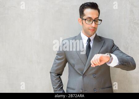Young handsome Persian businessman checking the time against concrete wall outdoors Stock Photo