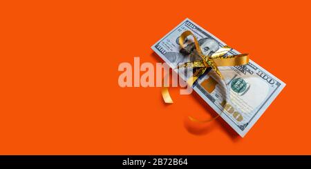 Stack of dollar banknotes with golden bow on orange background. Banner with copyspace concept Stock Photo