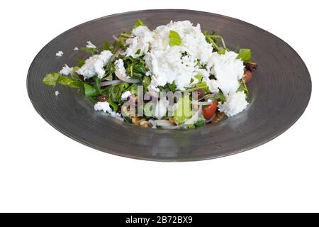 Salad plate with greens, olives, onions, walnuts and tomatoes topped with cheese in a restaurant Stock Photo