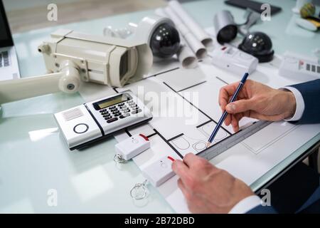 Architect Drawing Blueprint With Various Security Equipment On Desk Stock Photo