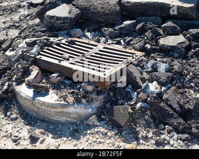 Road Demolition Debris, Metal Grill over Sewer Pipe, chunks of concrete and asphalt pavement, ground level, close-up view Stock Photo