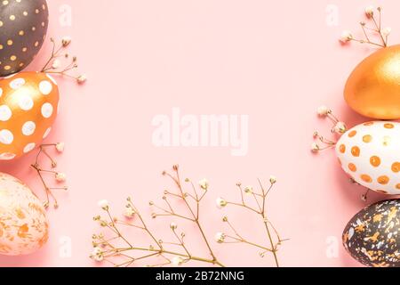 Top view of wooden painted eggs in gold, black and rose colors with branch of gypsophila on pink background. Happy easter mock up Stock Photo