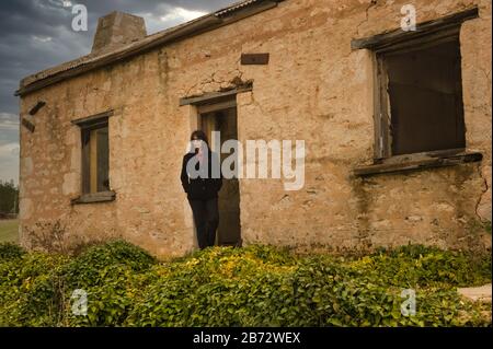 Female travelerstands in open doorway of an historic old settler hoestead in the Southern Flinders Ranges near Melrose in South Australia. Stock Photo