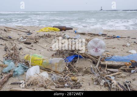 Spilled garbage on the beach of the big city. Empty used dirty plastic bottles, bags and other rubbish on the seashore. Stock Photo