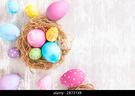 Easter eggs in nest and scattered over simple white wash wood tabletop - flat lay easter concept image with copy space for text. Stock Photo