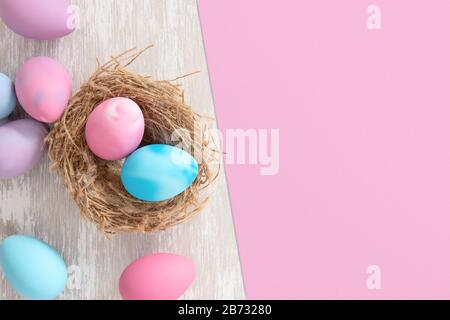 pastel pink and blue easter eggs in nest with pink paper split background for copy space - flat lay easter concept image Stock Photo
