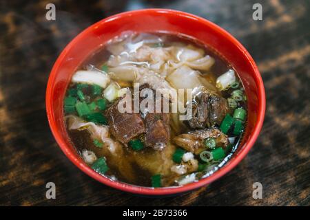 Close-up Taiwanese style handmade noodle with steamed beef stew and wontons in hot soup in red, black bowl, famous street food in Jiufen, Taiwan. Stock Photo