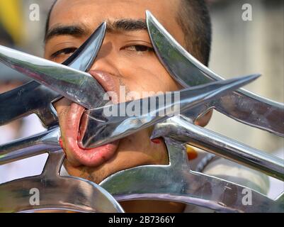 Thai Chinese Taoist devotee pierces his cheeks with two kung-fu halberds during the Phuket Vegetarian Festival (Nine Emperor Gods Festival). Stock Photo