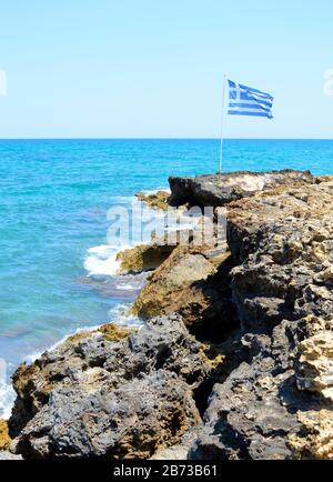 Kato Gouves coast in Crete the largest and most populated of the Greek islands flying the Greek national flag on the edge of the rugged coast Stock Photo