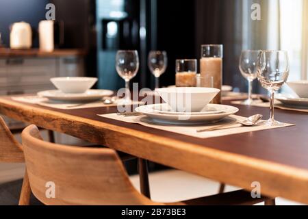 Elegant dinner table setting on a wooden table with dinnerware, silverware, utensil, wine glasses and candles. Table set for fine dining, luxury meal. Stock Photo