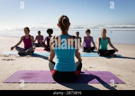 Rear view of yoga teacher doing a yoga session at the beach Stock Photo