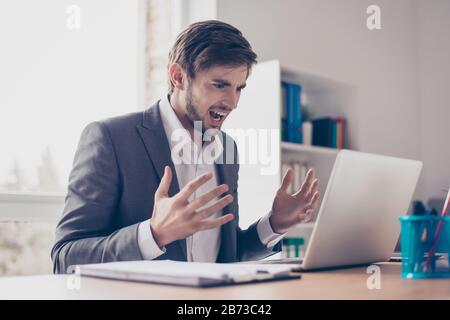 Angry young bearded businessman is sitting at a desk in the office, feeling nervous and making angry at his workstation. Stock Photo
