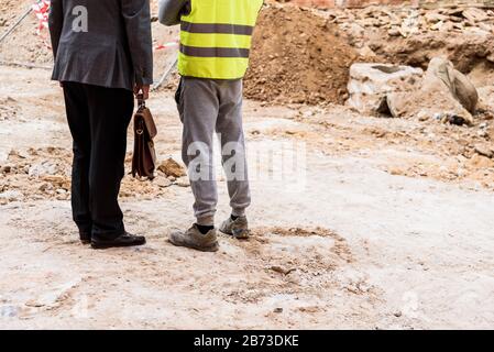 A bricklayer with his boss supervise the work of an excavator on a construction site. Stock Photo