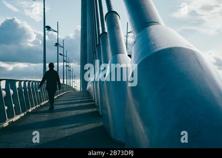 Person walks on an industrial bridge with large pylons and cable ties. Stock Photo