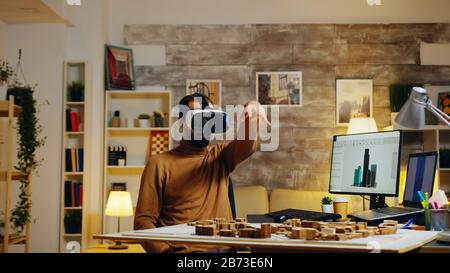 Young architect using virtual reality goggles modeling buildings in home office. Stock Photo