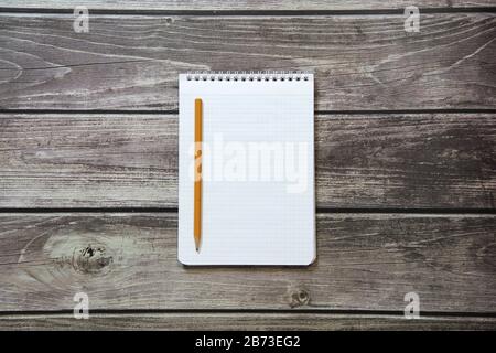 Notepad with a blank white sheet in a checker paper with simple graphite pencil lies on the background of wooden boards Stock Photo