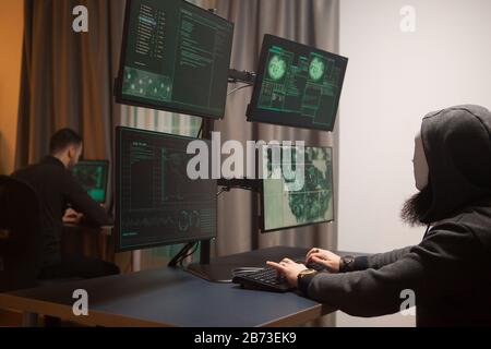 Masked and dangerous hacker in front of computer. Vulnerable government Stock Photo