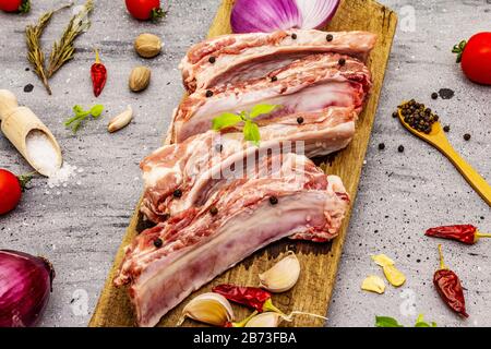 Raw pork ribs on grey stone concrete background. Round wooden cutting board, vegetables, spices and greens Stock Photo