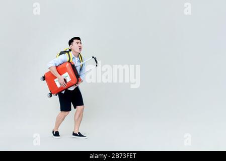 Shocked Asian tourist man holding luggage and looking upward isolated on gray background Stock Photo