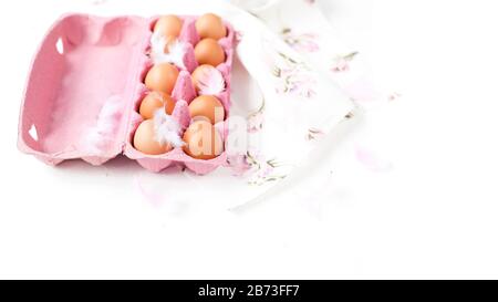 Close-up view of raw chicken eggs in egg pink box on white background. Decor and feathers. Free space for text. Banner Stock Photo