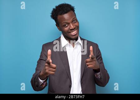Pleased dark skinned man points at you, chooses someone or advertises product. African American smiling male indicates at camera, isolated over blue b Stock Photo