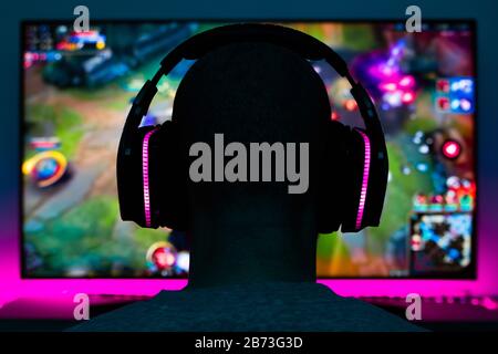 Stock photo of a gamer man with headphones playing a video game in front of the tv Stock Photo