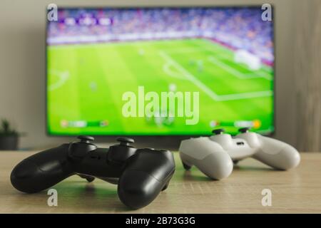 Stock photo of two gamepads on a table and a football game on TV in the background Stock Photo