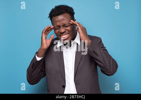Serious afro american young man with strict headache in studio on blue isolated background Stock Photo