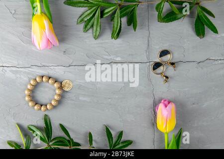 Jewelry, bracelet with keychain and gold earrings together with tulips and green laid on a concrete background. Inside the composition, free space Stock Photo