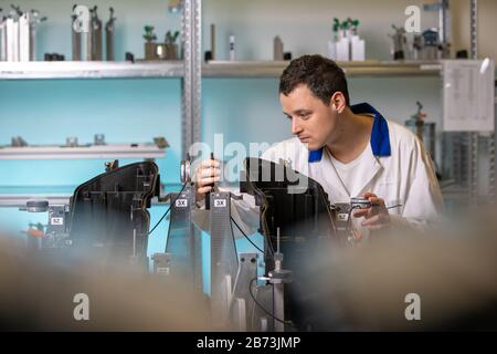 engineer measures plastic components for the production of lights for the automotive industry in a factory on a digital 3D machine Stock Photo