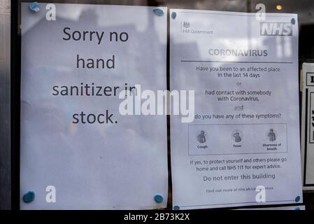 Westcliff on Sea, Essex, UK. 13th Mar, 2020. Printed signs on the window of a chemist detailing the symptoms of the Covid-19 Coronavirus alongside a notice advising customers that they have run out of hand sanitizer. The NHS warning notice is asking people with suspected symptoms not to enter the pharmacy. Product shortages Stock Photo