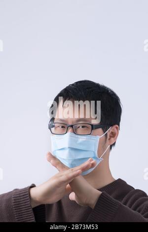 Portrait of young Asian man, saying no to coronavirus infection with wearing medical surgical blue face mask isolated on white background, close up, c Stock Photo