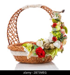 Brown wicker basket with original handle. Decor with flowers, eggs and a small ceramic bird. Made in a rustic style. Stock Photo