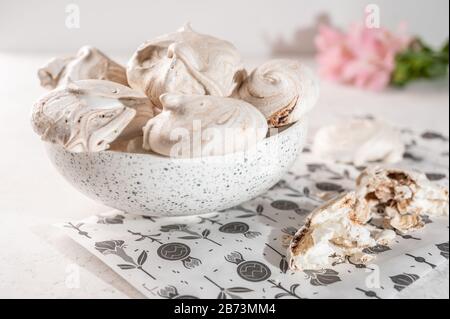 Homemade eggs dessert meringue on a plate on a light background. Next to pink flower and pieces of cookies. Copy space Stock Photo