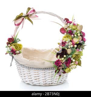 White wicker basket with fabric inside. Decorated with a variety of small flowers and eggs on a white background Stock Photo