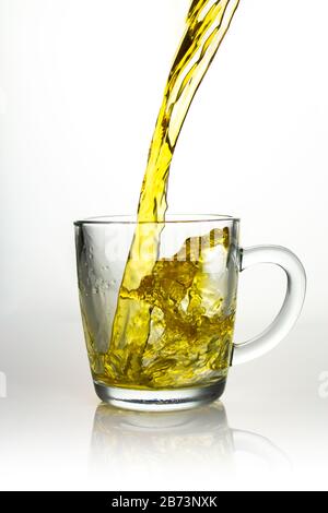 Splash of yellow tea in a transparent cup, pouring a transparent jet of tea with spray splashes, liquid drink beautiful juicy color with air bubbles a Stock Photo