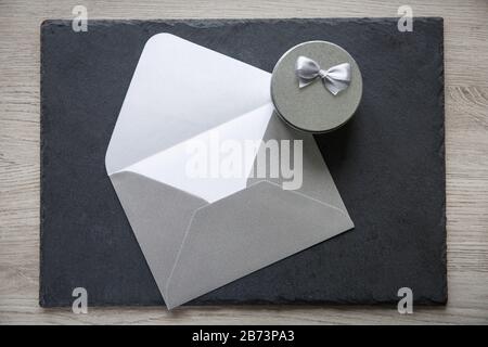 Letter envelope and small round silver gift box on black background. Celebration concept. Stock Photo