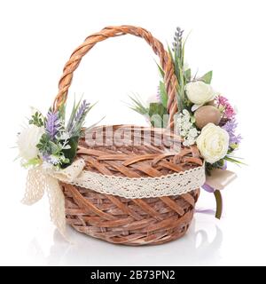 Beautiful large wicker basket with delicate flowers, lavender, greens and net. Decorated in a rustic style on white background Stock Photo