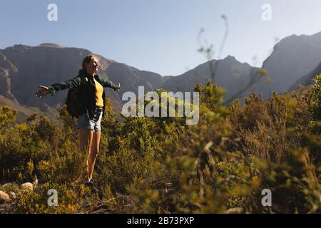 Side view of woman with backpack raising her arms in the air Stock Photo