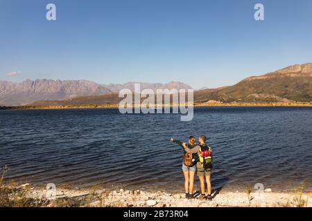 Rear view of couple with backpacks looking at the lake Stock Photo