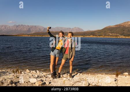 Front view of couple taking selfies in front of a lake Stock Photo