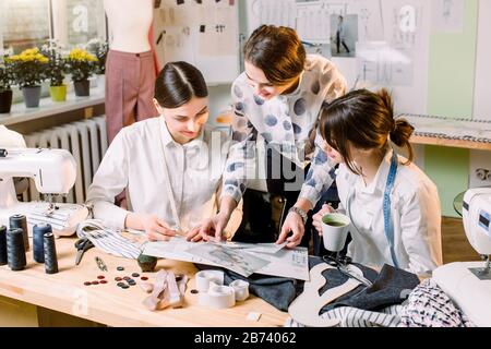 Three attractive young fashion designers carefully creating new fashionable styles of pants. Dressmakers making clothes. Fashion, dressmaker, sewing c Stock Photo