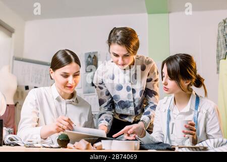 Three attractive young fashion designers carefully creating new fashionable styles of pants. Dressmakers making clothes. Fashion, dressmaker, sewing c Stock Photo