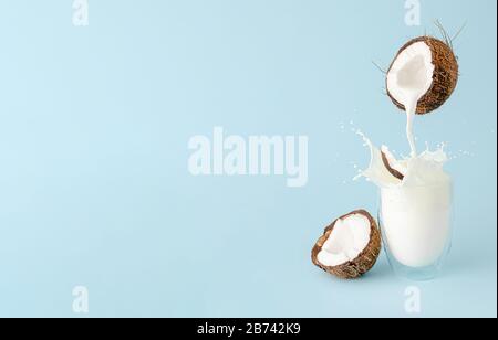 Pouring milk from a coconut and splash in a glass on pastel blue background. Food floating concept. Copy space Stock Photo