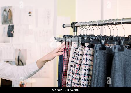 Closeup of womans hand selecting pants from rack in clothing shop. Close up of woman dressmaker hand choosing pants on clothes rack. Stock Photo