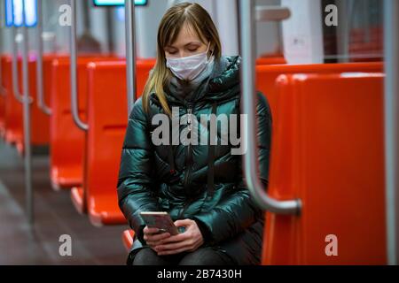 Woman in winter coat with protective mask on face sitting in subway car, using phone, looking worried. Preventive measures in public places Stock Photo