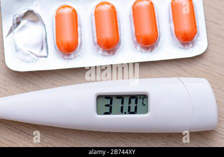 Close-up Thermometer showing high Temperature 37 and Pills on Table Stock Photo