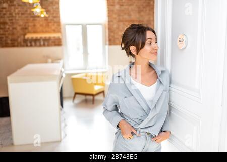 Woman regulating heating temperature with a modern wireless thermostat installed on the white wall at home. Smart home heating regulation concept Stock Photo