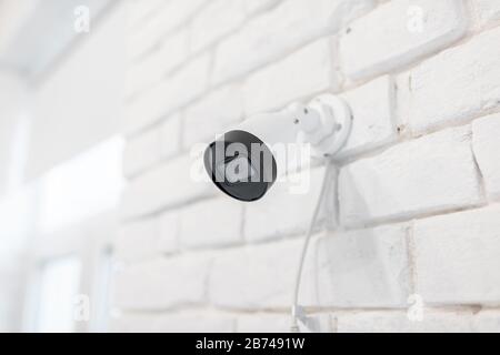 Surveillance ip camera mounted on the white brick wall indoors. Home video surveillance concept Stock Photo